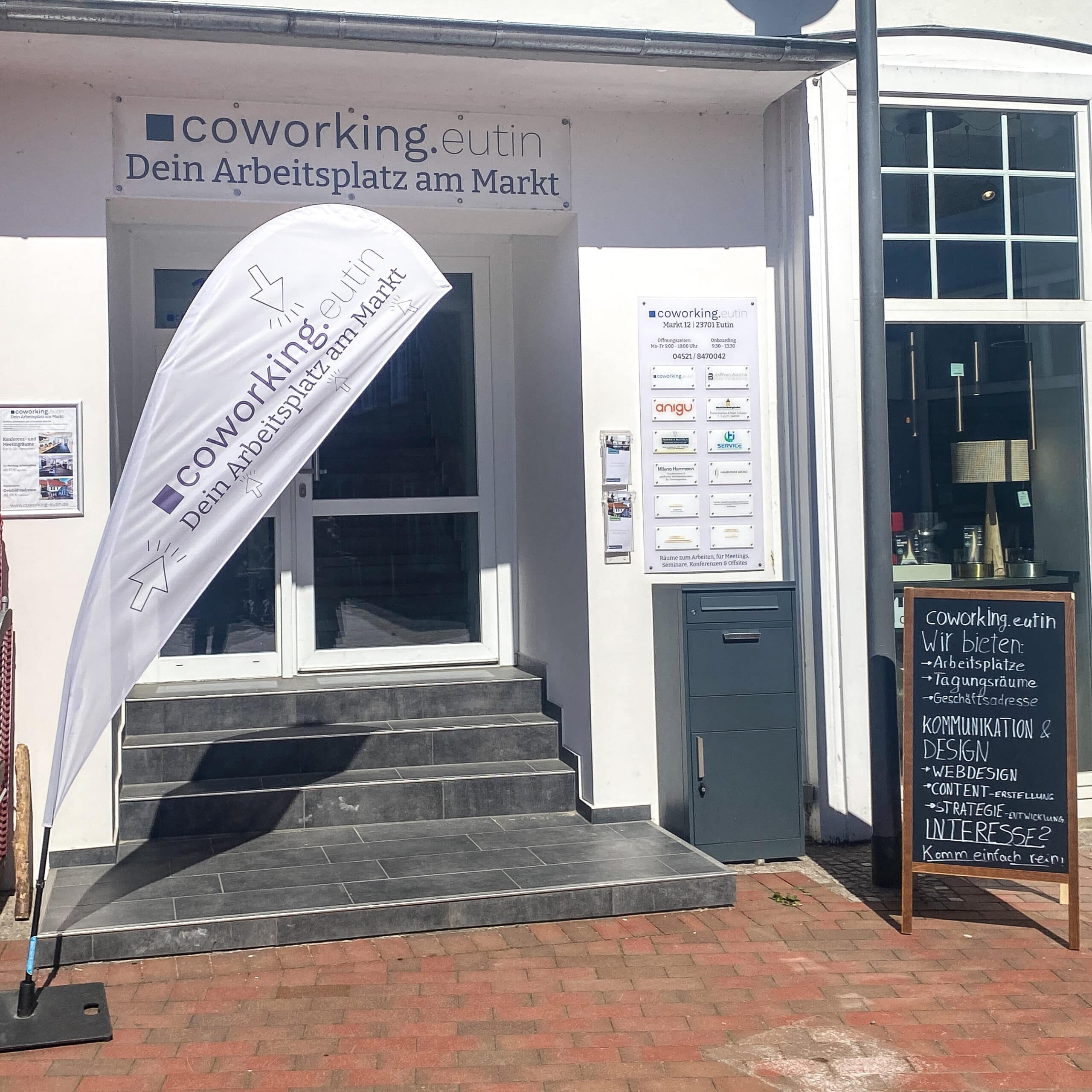 coworking eutin Eingsbereich mit Beachflag, Sammelbriefkasten und großer Schildertafel auf der die Logos der ansässigen Unternehmen sind.