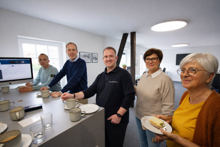 Organisatoren und Unternehmer beim gemeinsamen Unternehmerfrühstück Eutin. 6 Personen stehen an einem hohen Tisch in einem hellen freundlichen Raum.